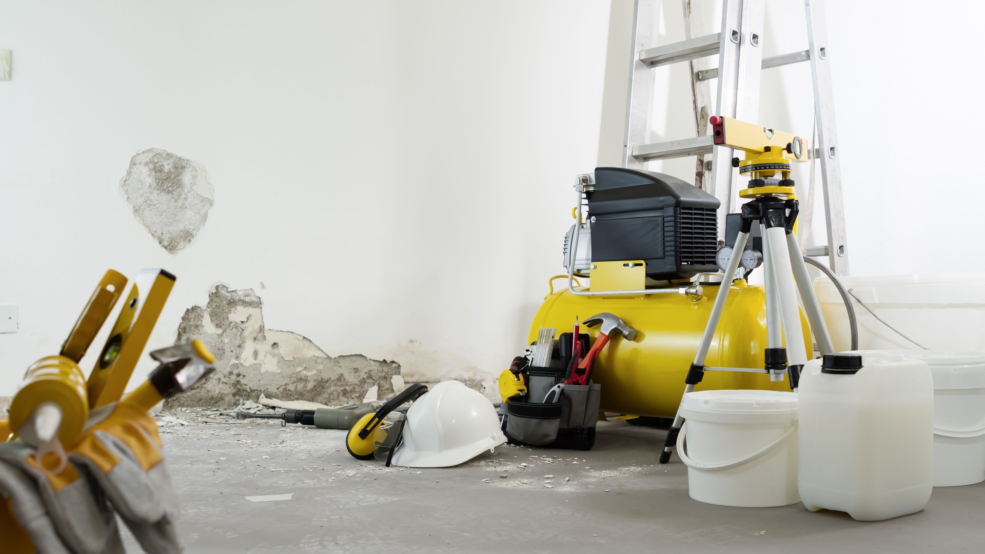 house renovation concept, helmet and safety headphones, air compressor and construction tools, white wall in the background